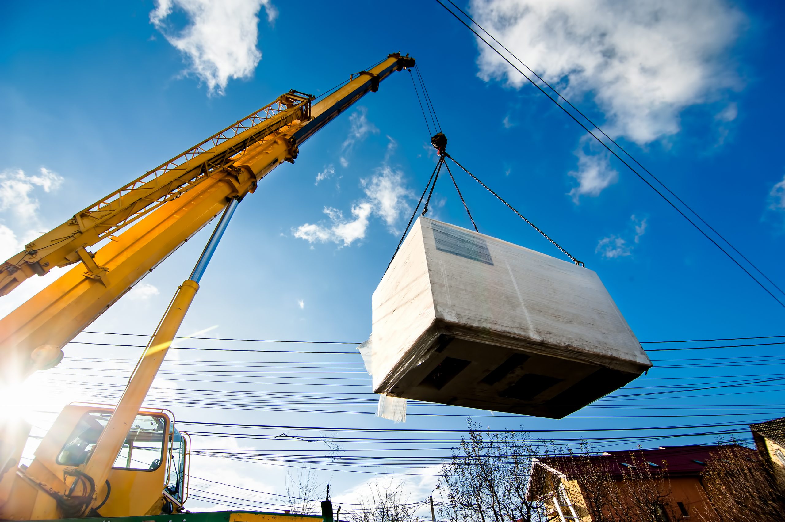 Crane lifting a transport crate with machine parts during the machinery relocation of the injection moulding machine
