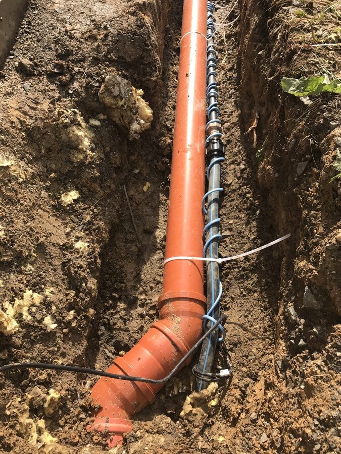 KG-Abwasserrohr und frostgeschützte Wasserleitung im ausgehobenen Graben