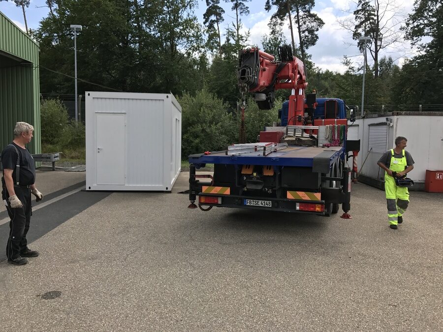 Containermodul schwebt am Ladekran zur Einbauposition