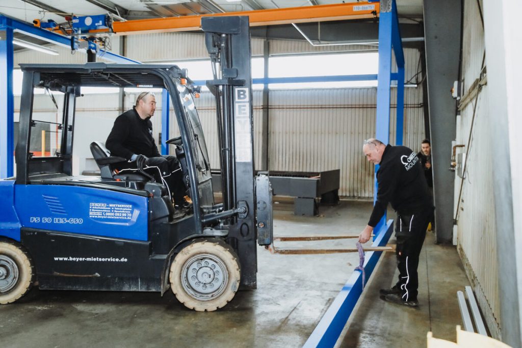 Teamarbeit beim Portalbau – Bahnträger wird per Stapler eingebracht und von Hand geführt