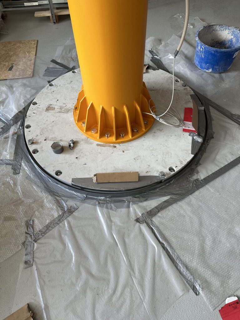 Säule des Schwenkkrans auf der verankerten Fußplatte, der fertige Hallenboden ist rundum mit Folie abgedeckt