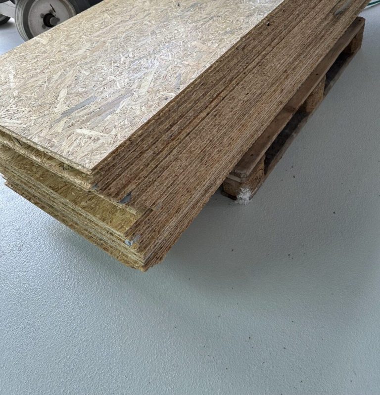Gestapelte Schutzplatten zum Abdecken des fertigen Hallenbodens vor Beginn der Montagearbeiten