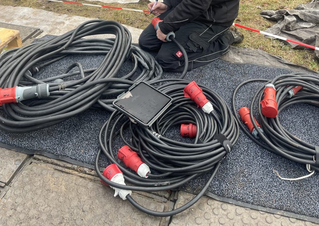 Aufgerollte Starkstromkabel mit roten CEE-Kupplungen, beschriftet mit Querschnitt und Länge, vor dem Verlegen auf der Baustelle