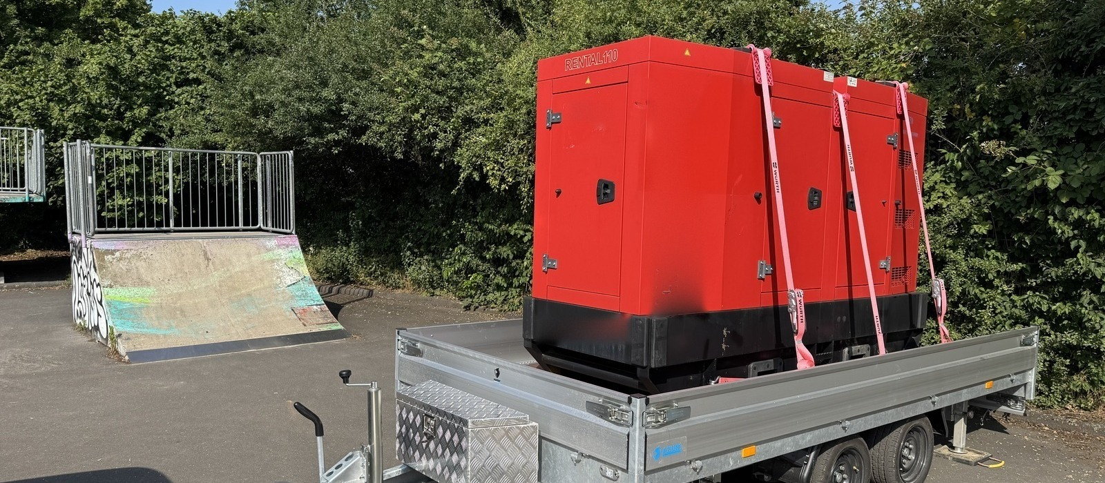 Schallgedämmtes 110-kVA-Stromaggregat auf einem Tandem-Anhänger, gesichert mit Spanngurten, bereit zur Auslieferung auf die Baustelle