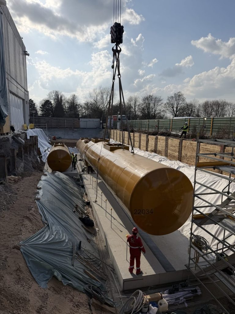 Dieseltank schwebt über der mit Folie ausgekleideten Grube kurz vor dem Absetzen
