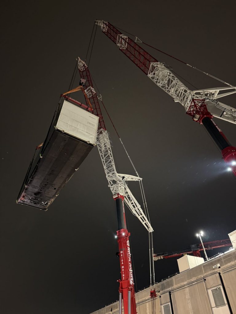 Tandemhub mit zwei Kranen: Containerlösung einer Netzersatzanlage über dem Gebäude