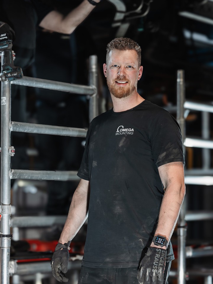 Tobias Schott, Geschäftsführer der Omega Mounting GmbH, auf einer Baustelle vor einem Gerüst